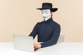 Hacker wearing vendetta mask sitting at the laptop and holding bak card