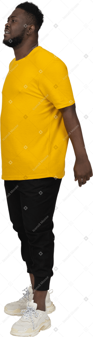Three-quarter view of a young dark-skinned man in yellow t-shirt holding hands behind
