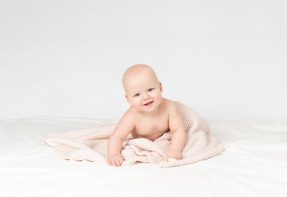 Bebé sonriente cubierto con una manta tejida de color beige