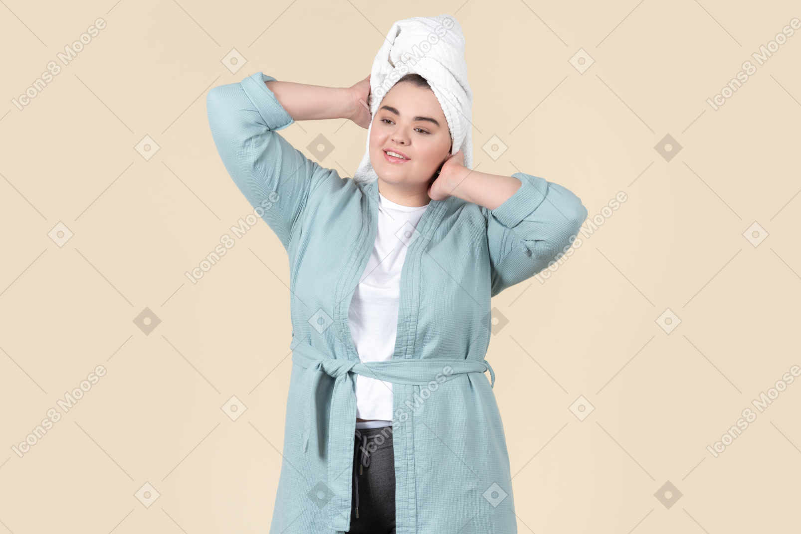Young plus-size woman in a light blue bathrobe and with a white towel on her head, standing against a plain beige background