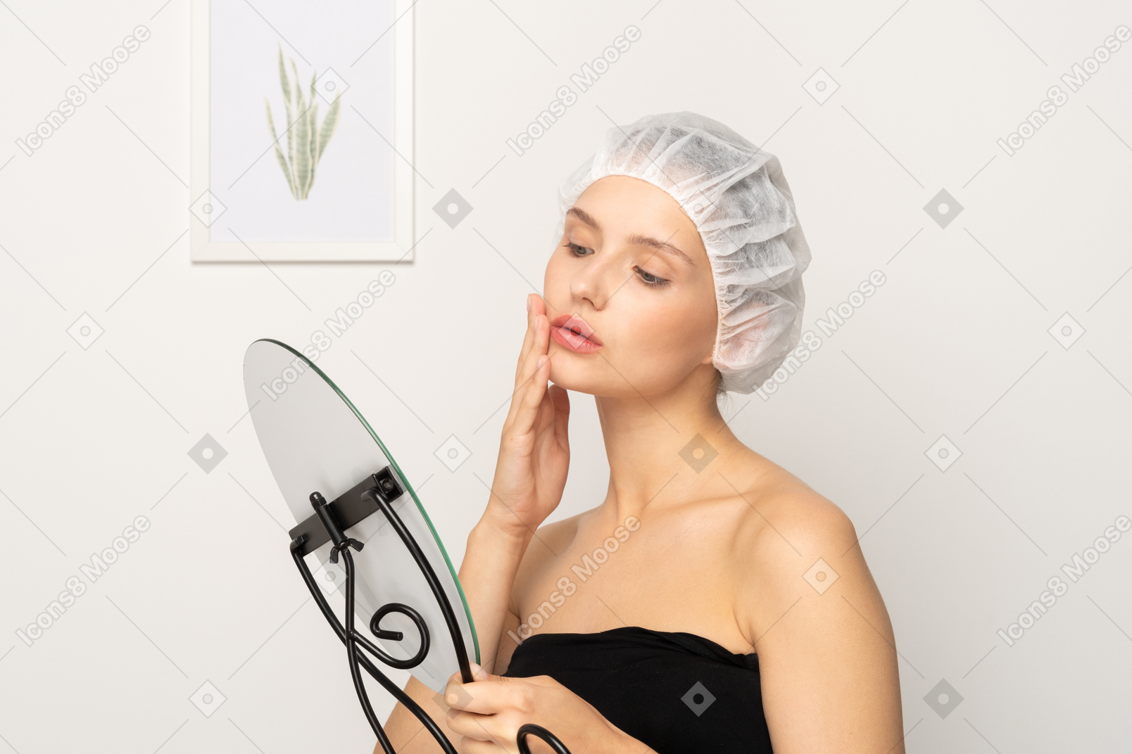 戴医用帽的年轻女病人照镜子时摸着自己的皮肤