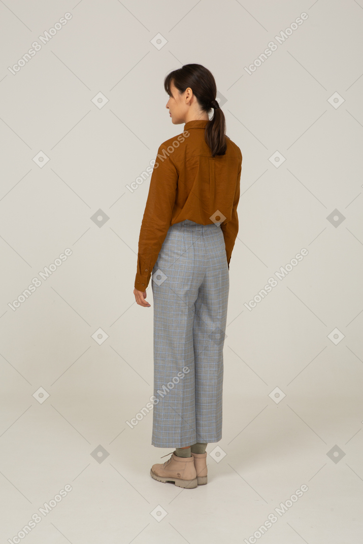 一位身着马裤和衬衫的年轻亚洲女性站在四分之三的后视图