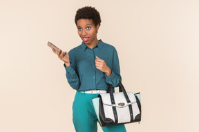 Doubting something young woman holding phone in one hand and bag on another