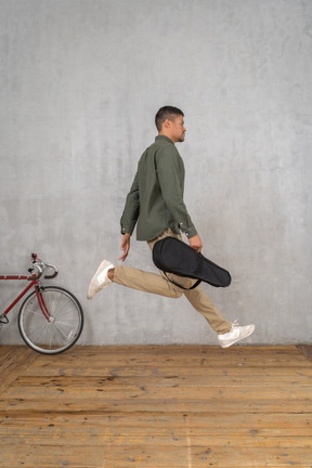 Side view of a man with a ukulele case jumping up