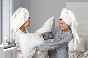 A couple of women in bathrobes fighting with pillows