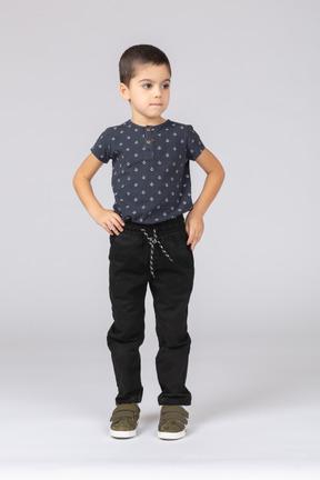 Vue de face d'un garçon mignon dans des vêtements décontractés posant avec les mains sur les hanches