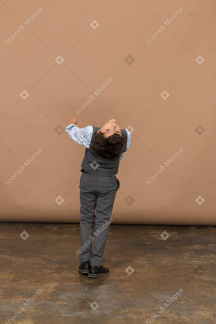 Vista traseira de um menino de terno cinza, dobrando e olhando para a câmera