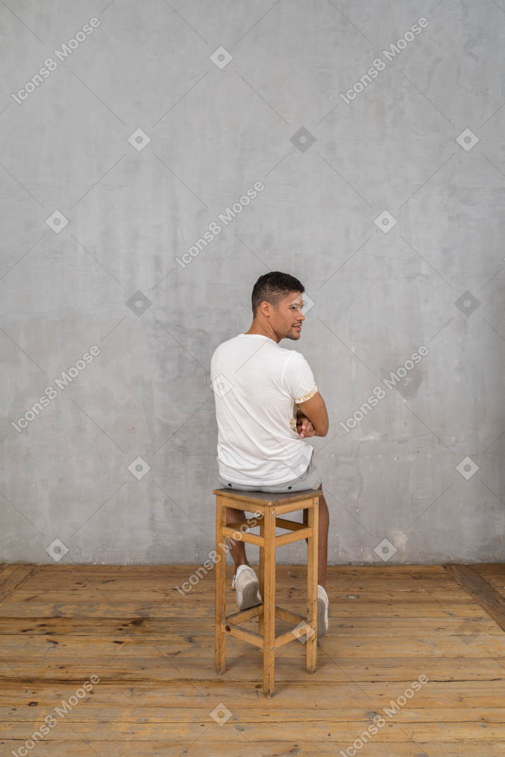 Rückansicht eines jungen mannes, der sitzt und zur seite schaut
