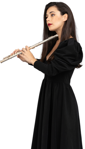 Vista lateral de uma jovem séria de vestido preto segurando uma flauta