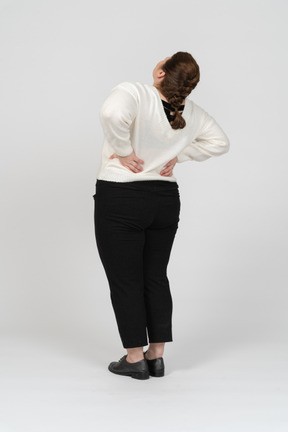 Vista posteriore di una donna grassoccia con un maglione bianco che soffre di dolore nella parte bassa della schiena