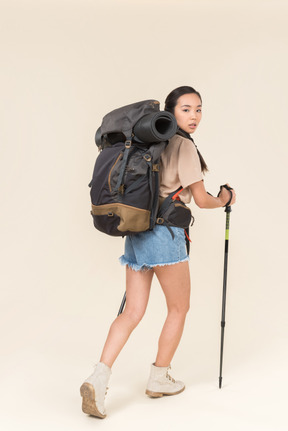 Young female asian hiker looking over shoulder and walking using trekking poles