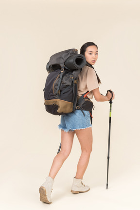 Joven mujer asiática excursionista mirando por encima del hombro y caminando con bastones de trekking