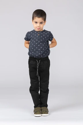 Front view of a cute boy standing with hands on back and looking at camera