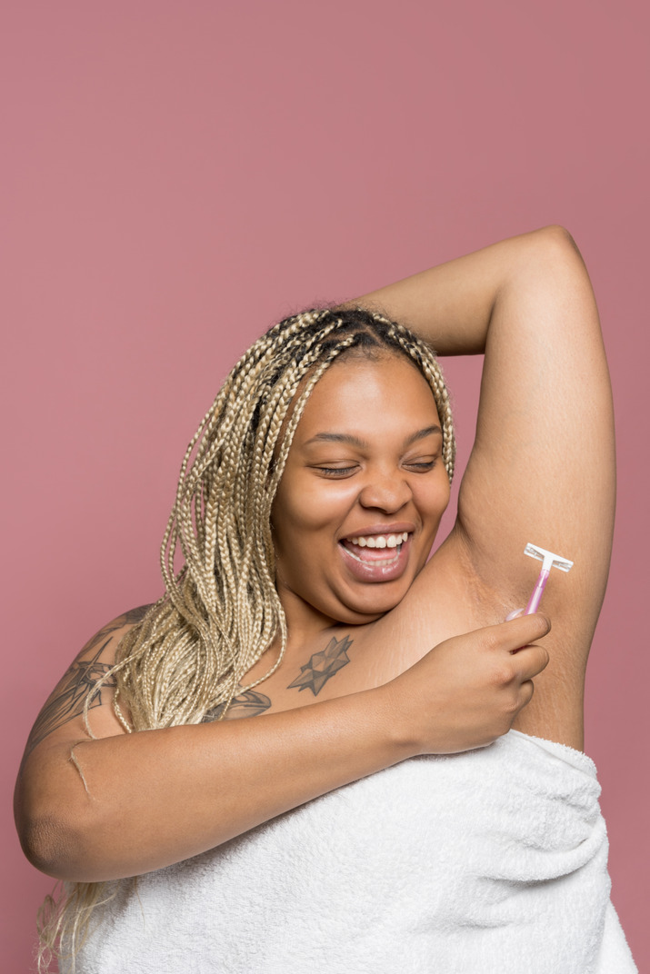 Cheerful african woman shaving underarms