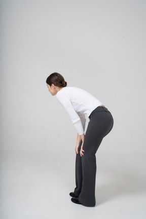 Vista laterale di una donna in pantaloni neri e camicetta bianca che si china
