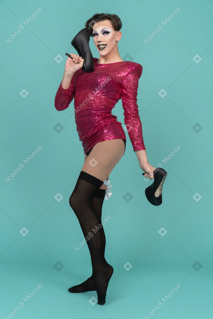 Drag queen smiling while holding high-heel shoes