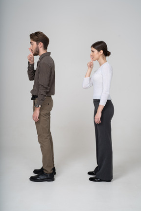 沈黙のジェスチャーを示す事務服の若いカップルの側面図