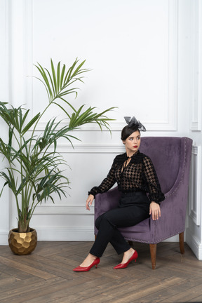 Woman sitting in fancy armchair next to houseplant