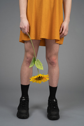 Zugeschnittenes foto einer person in orangefarbenem kleid, die eine sonnenblume hält