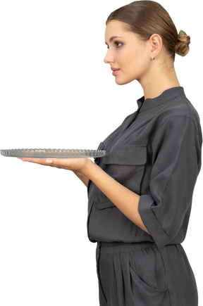 Вид сбоку молодой женщины в комбинезоне, держащей стеклянную тарелку