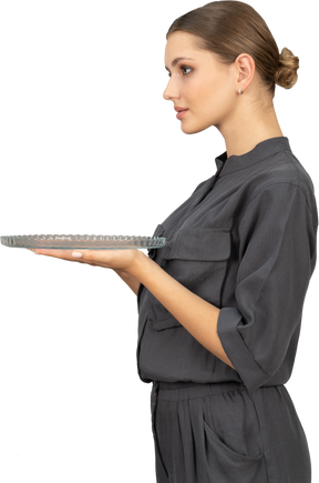 Side view of a young woman in a jumpsuit holding glass plate