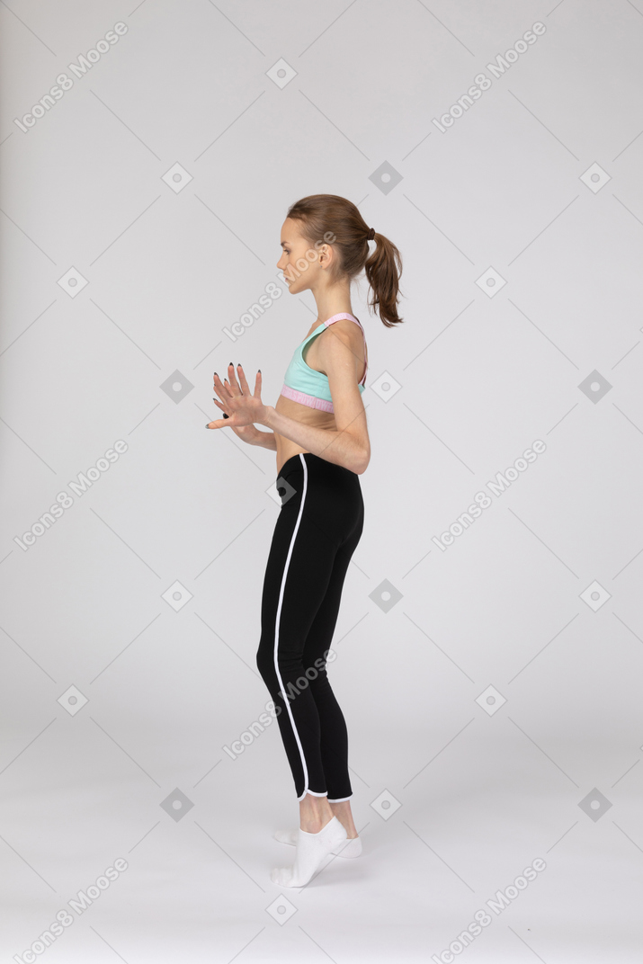 一个十几岁的女孩在打手势时跳舞的运动服的侧视图