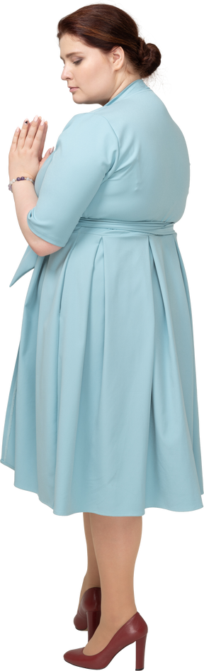 Vista laterale di una donna in abito blu che fa un gesto di preghiera