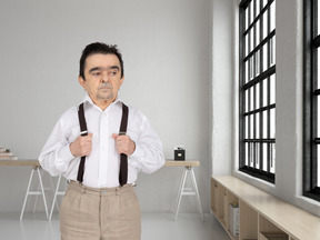 A man in a white shirt and brown suspenders looking at the window