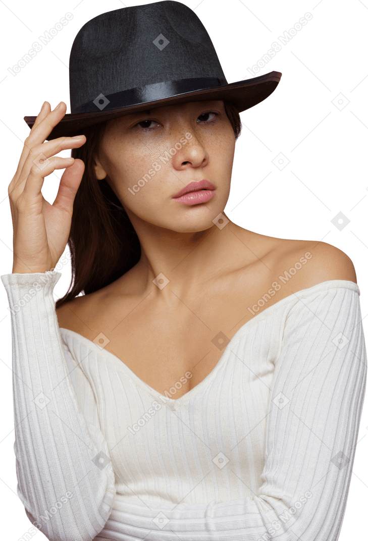 Vista frontal de una joven mandona tocando elegantemente su sombrero negro