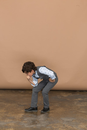 Vista frontal de un niño en traje en cuclillas y sosteniendo el puño en la barbilla