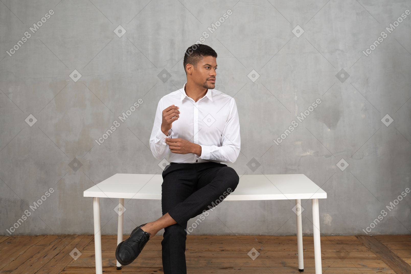 Uomo in abiti formali seduto su un tavolo e che si fissa il polsino