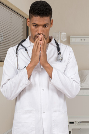 A man in a white lab coat is holding his hands together