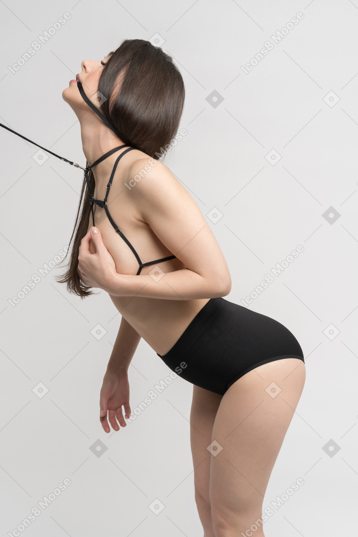 Side view of sexy young woman in harness and leash