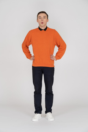 Молодой человек в оранжевом свитере стоит