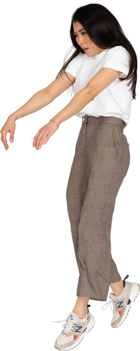 Vista di tre quarti di una giovane donna in calzoni e t-shirt con le mani tese