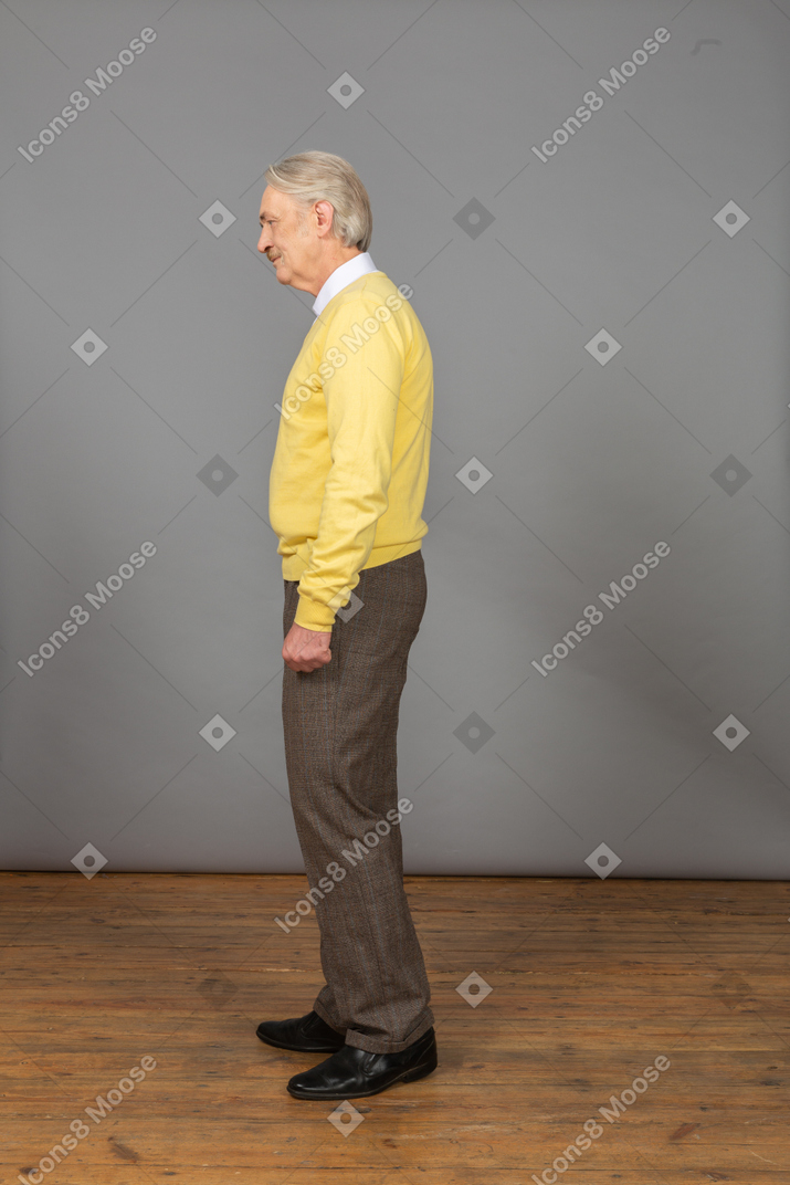 Vista lateral de um velho deprimido vestindo um pulôver amarelo e olhando para o lado