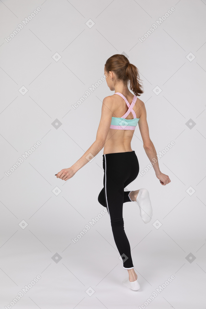 一个十几岁的女孩，在运动服，抬高腿的四分之三后视图