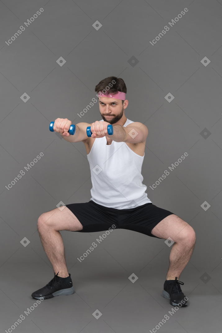 Homme faisant squat avec ses bras tendus et tenant des haltères