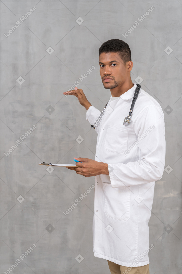 Young doctor with stethoscope holding clipboard and gesturing