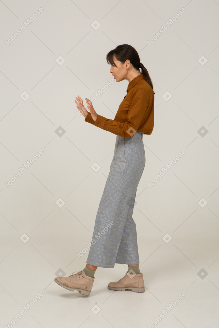 Vista laterale di un'attenta giovane donna asiatica in calzoni e camicetta che allunga le braccia