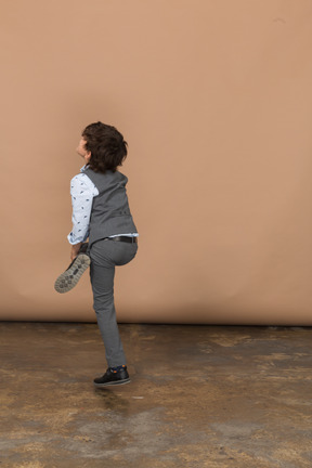 一个穿着西装的男孩单腿站立的侧视图