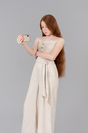 Teenage girl dressed in beige overalls making a selfie with smartphone