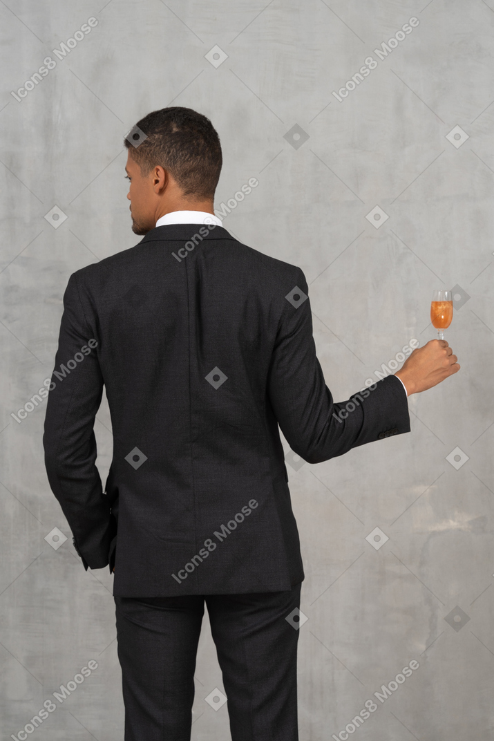 Vista trasera del joven sosteniendo una copa de champán y mirando a un lado