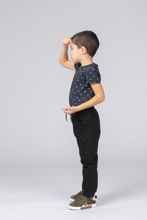 Вид сбоку мальчика в повседневной одежде, позирующего с рукой на голове