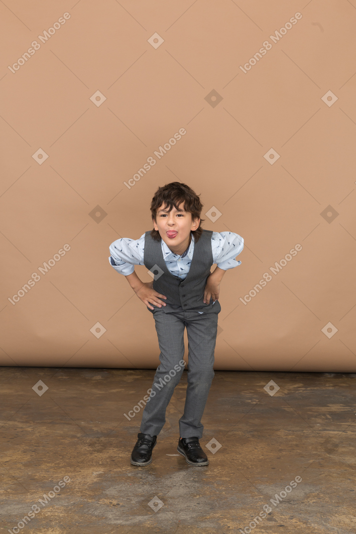 Vista frontal de um menino de terno em pé com as mãos nos quadris e curvando-se