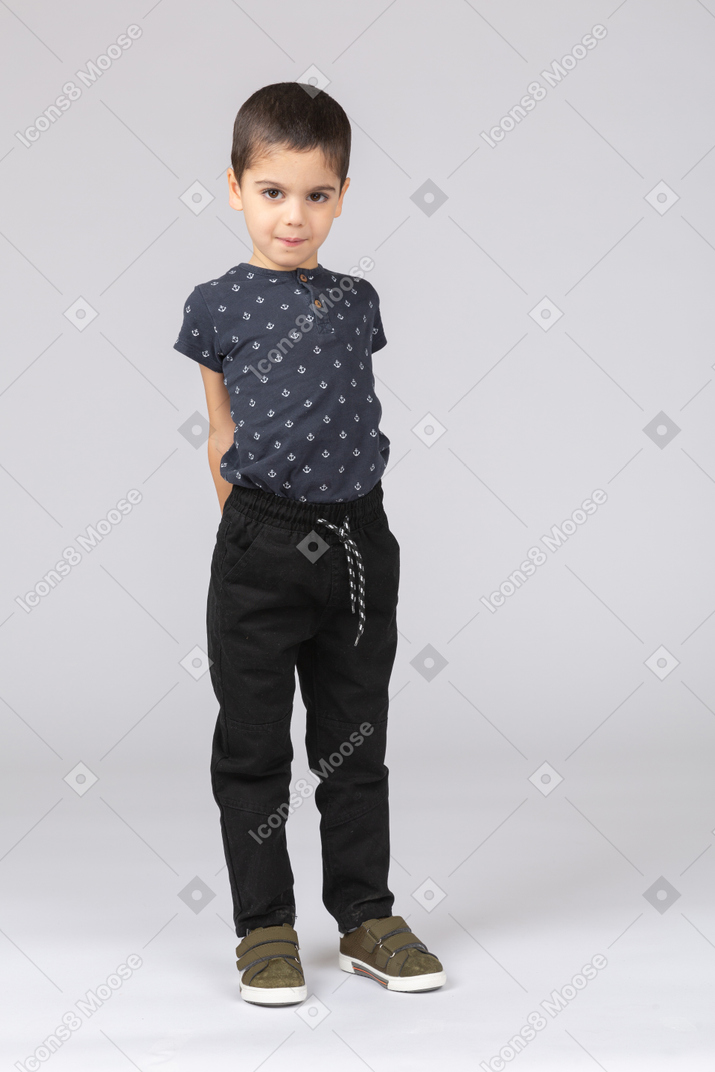 Front view of a cute boy posing with arms behind back and looking at camera