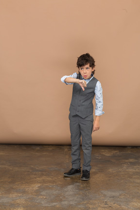 Vista frontal de un niño con traje gris que muestra el pulgar hacia abajo