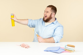 Laughing young overweight househusband holding cleaning spray and rags