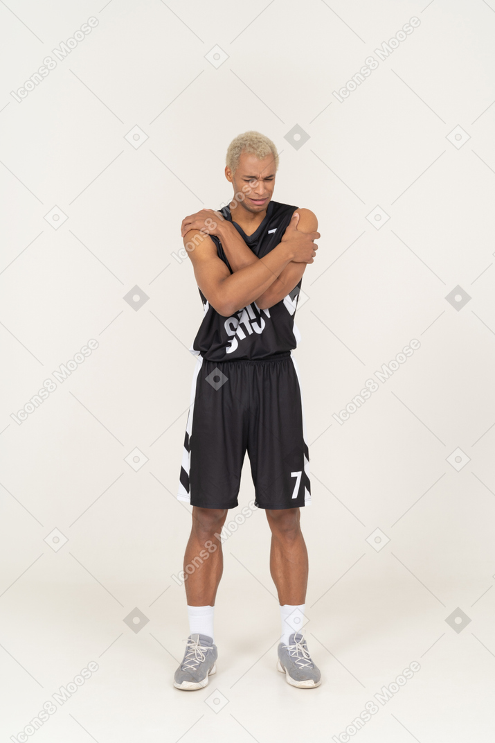 Front view of a withdrawn young male basketball player embracing himself