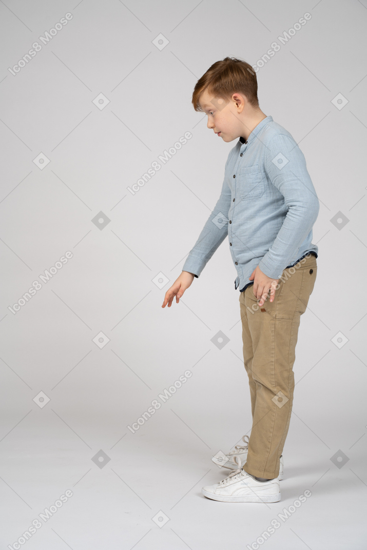 Young boy in blue shirt and khaki pants reaching down
